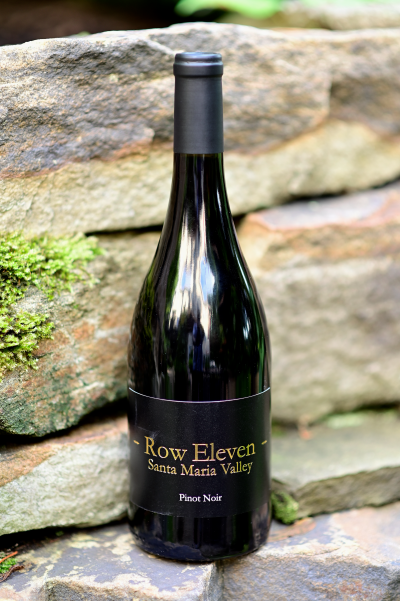 Photo of a bottle of Row Eleven Santa Maria Valley Pinot Noir sitting on stone wall.